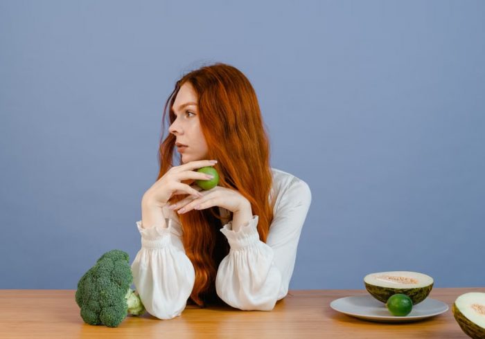Thoughtful woman with broccoli, melon, and lime on a table.